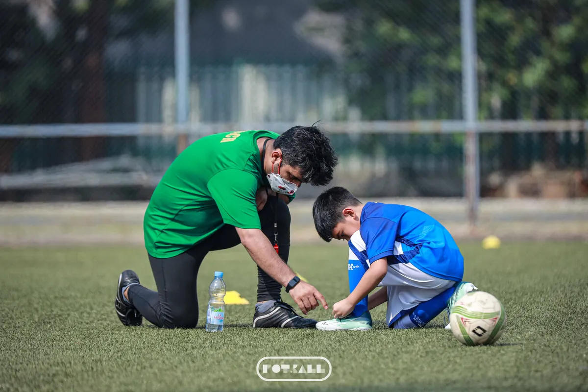 Pelatih membantu mengikat tali sepatu murid sebelum latihan